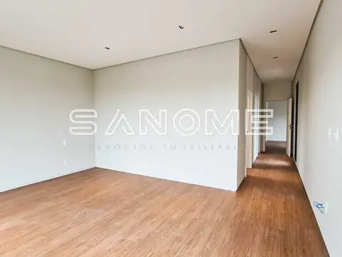 Sala vazia com piso de madeira e acesso ao corredor