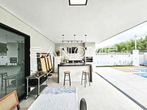 Área de lazer com cozinha, bancada e piscina ao fundo