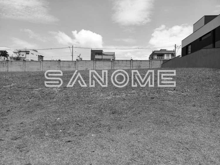 Terreno vazio com muro de concreto e edificações ao fundo
