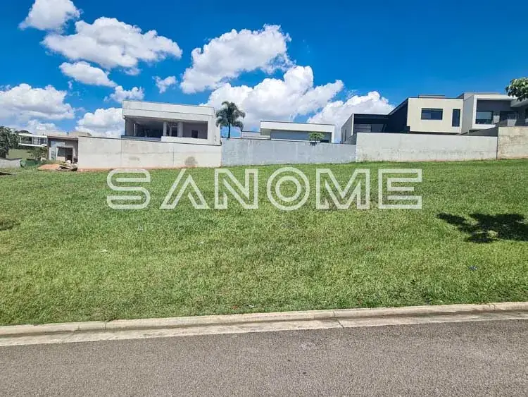 Terreno com grama e casarões ao fundo