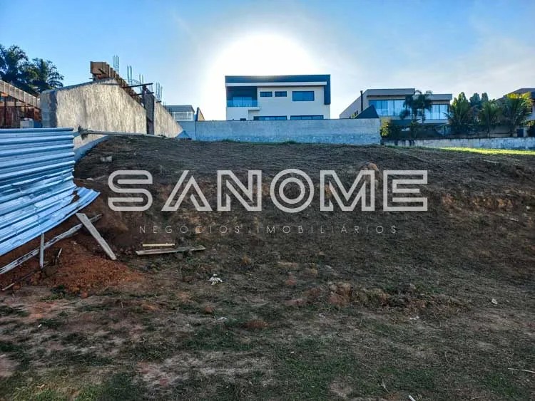 Terreno com placa de imobiliária e construções ao fundo