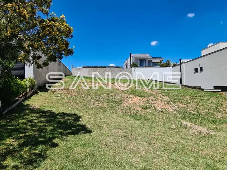 Terreno com grama e casarões ao fundo sob céu azul
