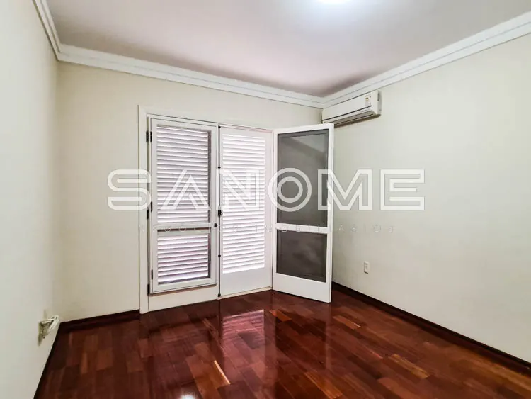 Quarto vazio com piso de madeira e portas com venezianas