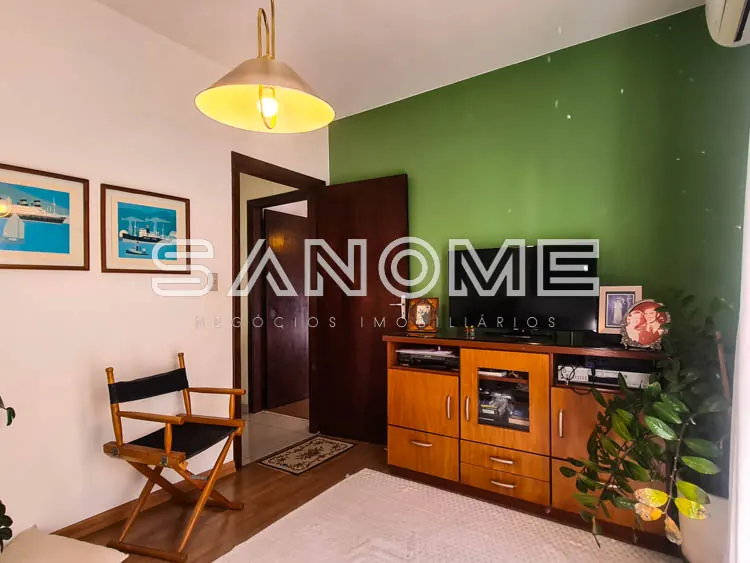 Sala com parede verde, móvel de madeira e luminária dourada